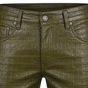 Puede incluir: Pantalones de color verde oliva con una textura brillante en relieve que imita la piel de cocodrilo. La prenda incluye una cintura estándar con cierre de botón central, trabillas para cinturón, dos bolsillos delanteros y remaches.