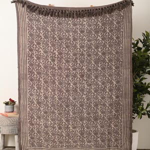 Könnte beinhalten: Rechteckige Decke mit braunem und beigem Blumenmuster. Die Decke hat einen Fransenbesatz am unteren Rand und einen gestreiften Rand. Der obere Rand hat ebenfalls Fransen. Ideal für ein Bett oder Sofa.