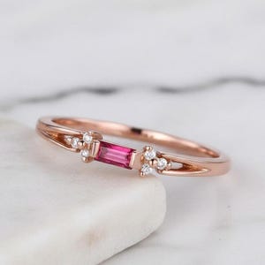Peut inclure: Bague en or rose ornée d'une pierre rose rectangulaire au centre, flanquée de petits brillants blancs. La monture présente un design délicat et ajouré. Un bijou.
