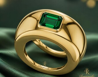 May include: A wide, polished gold band ring featuring a single emerald-cut green gemstone set in the center. The interior of the band is engraved with the text Rayajewells, and the same brand name is printed in the lower right corner of the image.