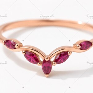 Peut inclure: Une bague en or rose dotée d'un anneau en forme de V serti de cinq rubis rose foncé taille marquise. Les pierres sont disposées de manière symétrique sur le dessus de l'anneau, avec une pierre centrale et deux pierres de chaque côté.