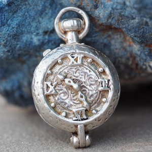 May include: A silver charm in the shape of a pocket watch with Roman numeral markings on the face.