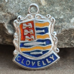May include: Silver charm with a blue, yellow, and red enamel coat of arms with the word "CLOVELLY" in blue enamel.