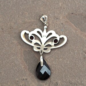 May include: Silver pendant with a black gemstone drop and two smaller red gemstones. The pendant is in the shape of a stylized butterfly with intricate details.