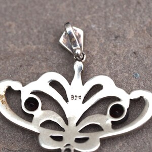 May include: Silver pendant with a delicate butterfly design featuring two red gemstones and a 925 hallmark.