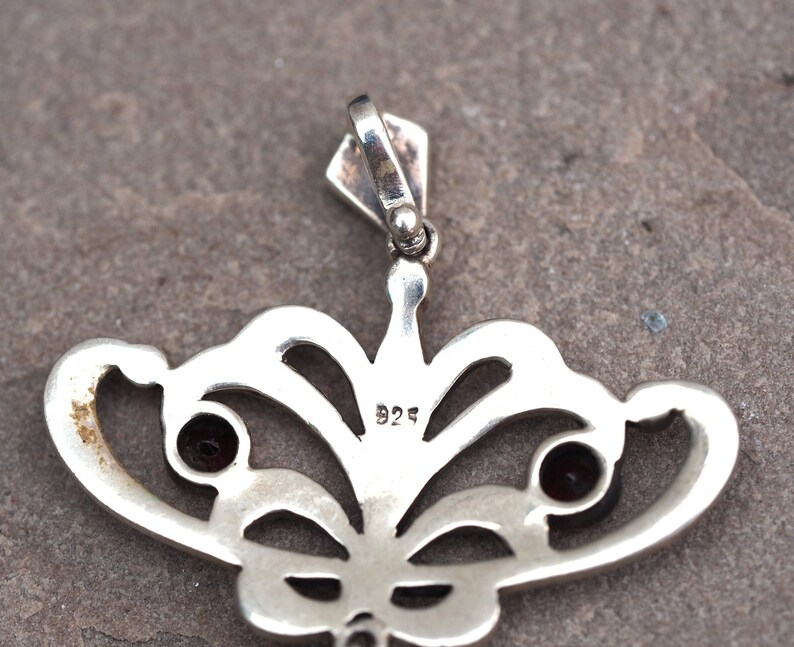 May include: Silver pendant with a delicate butterfly design featuring two red gemstones and a 925 hallmark.