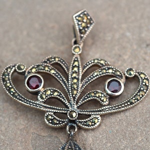 May include: A silver pendant with a delicate, ornate design featuring two red gemstones and a marcasite finish.