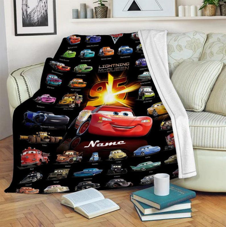 May include: A black fleece blanket featuring a repeating pattern of various Cars characters, a large central red Lightning McQueen graphic with the number 95, and the word Name in white script. The blanket has a white plush underside.