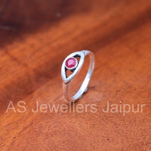 May include: A silver ring with a red gemstone set in an eye-shaped design. The ring is on a wooden surface. The text "AS Jewellers Jaipur" is at the bottom of the image.