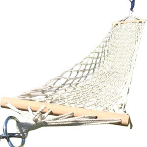 May include: A white, woven hammock with a wooden spreader bar and a metal ring for hanging. The hammock is suspended from a blue rope and is designed for outdoor relaxation. The net-like weave provides breathability.