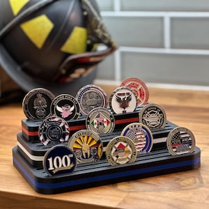 May include: A display stand holding a collection of commemorative coins. The coins feature various designs and emblems, including a pink pig, a firefighter's helmet, and the text "100". The stand is black with red and blue stripes.