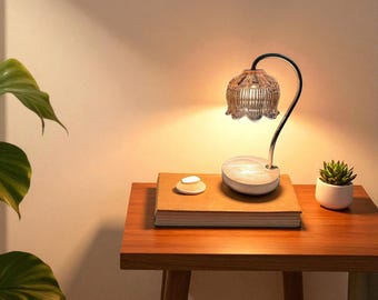 May include: A decorative table lamp with a clear, flower-shaped glass shade and a curved metal arm. The lamp sits on a wooden base, next to a small succulent plant in a white pot. A book and a small, white, ceramic object are also on the table.