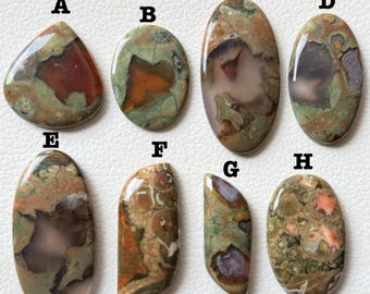 May include: Eight polished gemstone cabochons in various shapes, including oval, teardrop, and irregular forms. The stones display a mix of earthy tones, with shades of brown, green, and red. Each stone has unique patterns and textures, suitable for jewelry making or collecting.