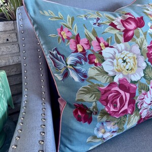 Puede incluir: Una almohada azul con un patr&oacute;n floral con flores rosas, rojas y blancas. La almohada tiene un ribete rosa alrededor de los bordes.