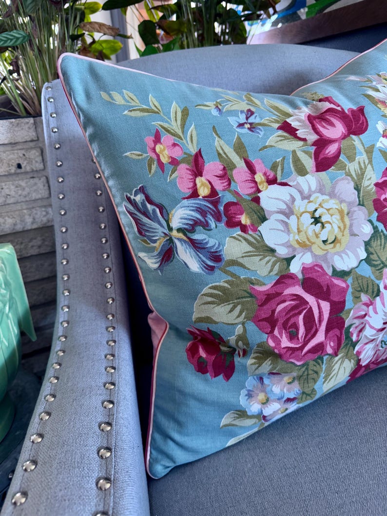 Puede incluir: Una almohada azul con un patr&oacute;n floral con flores rosas, rojas y blancas. La almohada tiene un ribete rosa alrededor de los bordes.