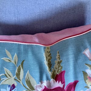 Puede incluir: Una almohada azul y rosa con un patr&oacute;n floral. La almohada tiene un borde blanco y un borde rosa.