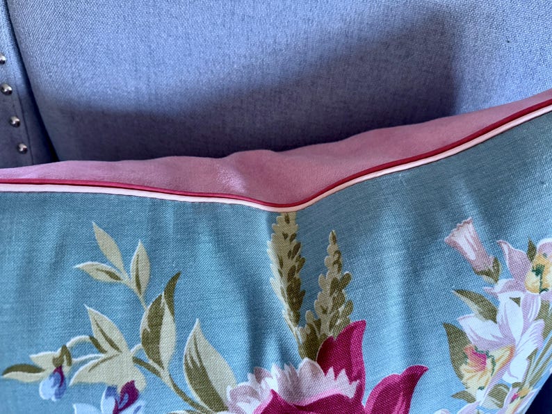 Puede incluir: Una almohada azul y rosa con un patr&oacute;n floral. La almohada tiene un borde blanco y un borde rosa.