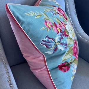Puede incluir: Una almohada floral azul y rosa con ribete blanco. La almohada est&aacute; sentada en una silla azul claro con tachuelas plateadas.