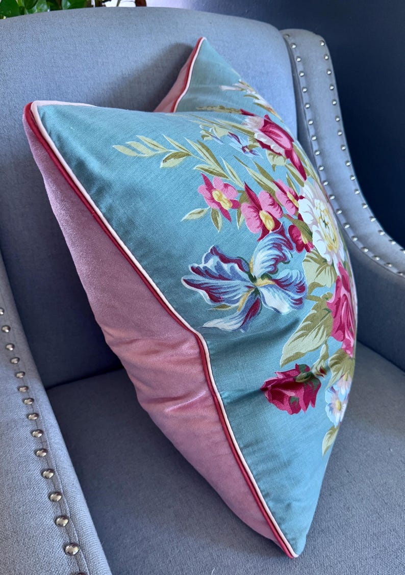 Puede incluir: Una almohada floral azul y rosa con ribete blanco. La almohada est&aacute; sentada en una silla azul claro con tachuelas plateadas.