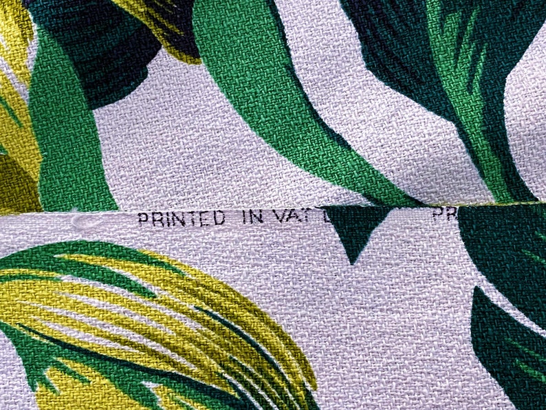 K&ouml;nnte beinhalten: Nahaufnahme eines wei&szlig;en Stoffes mit einem Muster aus gr&uuml;nen und gelben Bl&auml;ttern. Der Stoff hat eine strukturierte Webart und der Text "PRINTED IN VATIC" ist sichtbar.