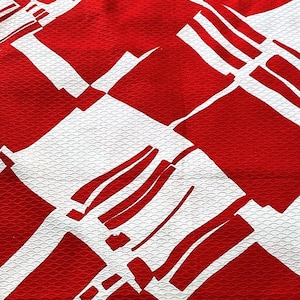 May include: Red and white fabric with a geometric pattern. The fabric has a textured surface.