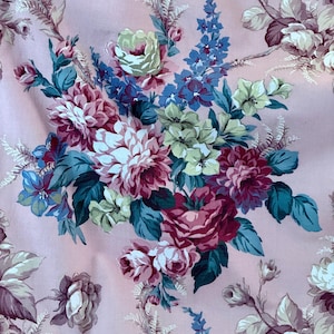 May include: A floral fabric with a repeating pattern of large, colourful blooms. The flowers are in shades of pink, burgundy, blue, and green, set against a pale pink background. The design includes roses, dahlias, and other floral elements.
