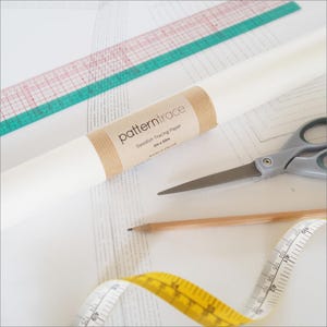 May include: A roll of white pattern tracing paper with a brown paper band, scissors, a pencil, a ruler, and a yellow measuring tape. The paper is labelled "pattern trace" and "Swedish Tracing Paper 1m x 10m".