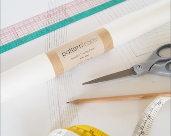 Op de afbeelding: Een rol wit patroonpapier met een bruine papieren band, een schaar, een potlood, een liniaal en een gele meetlint. Het papier is gelabeld met "pattern trace" en "Swedish Tracing Paper 1m x 10m".