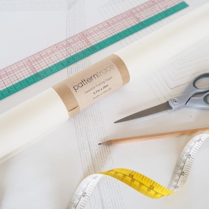 May include: A crafting setup with a roll of "patterntrace" Swedish tracing paper, a pink and green ruler, scissors, a pencil, and a yellow measuring tape. The paper roll is 0.7m x 20m, made in the UK.