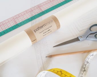 Op de afbeelding: Een naaiscène met een rol "patterntrace" Zweeds traceerpapier, een roze en groene liniaal, een schaar, een potlood en een geel meetlint. De papierrol is 0,7 m x 20 m groot en gemaakt in het VK.
