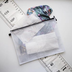 Puede incluir: Una bolsa transparente con cremallera que contiene patrones de costura y tela, con una tela estampada floral y una regla blanca con marcas negras. La regla muestra medidas de hasta 120 pulgadas (304,8 cm).