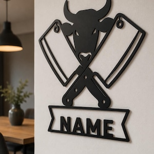 May include: A black wall-mounted sign featuring a stylised bull head silhouette positioned above two crossed meat cleavers. Below the cleavers is a horizontal banner with the word NAME cut out in bold, capital, sans-serif lettering.