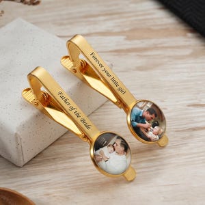 May include: Two gold-colored tie clips with engraved text and photo inserts. One clip reads "Father of the Bride," the other "Forever your little girl." Each clip features a circular photo of a father and child.
