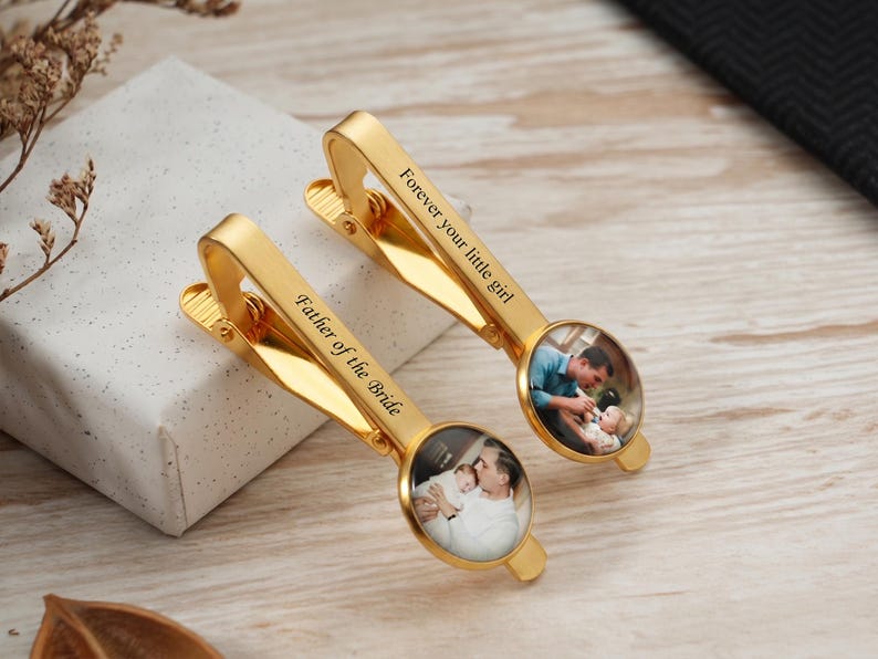 May include: Two gold-colored tie clips with engraved text and photo inserts. One clip reads "Father of the Bride," the other "Forever your little girl." Each clip features a circular photo of a father and child.