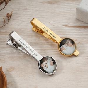 May include: Two personalized tie clips, one gold and one silver, each featuring a small circular photo. The gold clip reads "I love you dad," and the silver clip reads "Forever your baby girl."