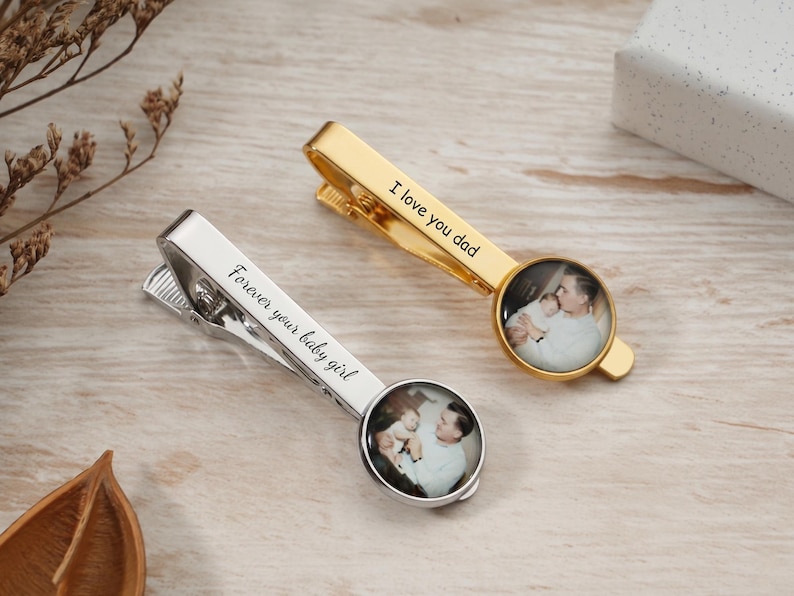 May include: Two personalized tie clips, one gold and one silver, each featuring a small circular photo. The gold clip reads "I love you dad," and the silver clip reads "Forever your baby girl."