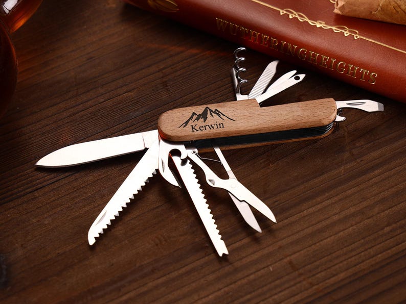 Puede incluir: Una multiherramienta con mango de madera y varios implementos de acero inoxidable, incluyendo un cuchillo, sierra, tijeras y sacacorchos. El mango est&aacute; grabado con un dise&ntilde;o de monta&ntilde;a y el nombre "Kerwin".