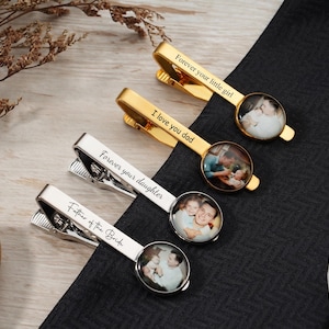 Puede incluir: Cuatro pasadores de corbata personalizados con insertos fotográficos. Dos son dorados y dos plateados. Los clips dorados tienen las frases "Forever your little girl" e "I love you dad". Los clips plateados dicen "Forever your daughter" y "Father of the Bride".