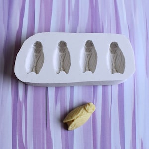 Peut inclure: Un moule en silicone blanc avec quatre formes de cigales. Une seule cigale jaune est placée sous le moule.