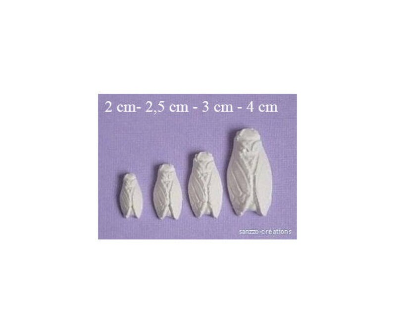 May include: Four white cicada-shaped decorations of varying sizes, ranging from 2 cm to 4 cm in length, are displayed on a lavender background. The decorations have detailed wing and body patterns. The text "2 cm - 2,5 cm - 3 cm - 4 cm" is at the top.