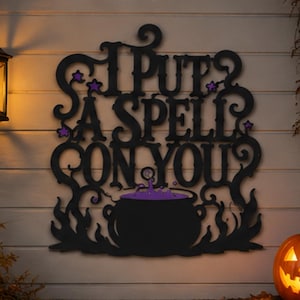 Könnte beinhalten: Ein schwarzes Wandschild mit dem Text I PUT A SPELL ON YOU in einer dekorativen Schriftart, akzentuiert durch kleine violette Sterne. Unter dem Text befindet sich ein schwarzer Kessel mit blubbernder violetter Flüssigkeit, umgeben von stilisierten schwarzen Flammen.