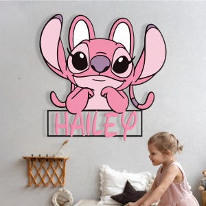 May include: A pink cartoon character wall decoration with the name "HAILEY" in pink letters. The character has large ears and is smiling. The decoration is mounted on a light grey wall.