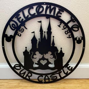 May include: Black metal wall art with the words "WELCOME TO OUR CASTLE" and "EST 1989" in a circular design. The artwork features a castle silhouette, Mickey and Minnie Mouse, and a heart.