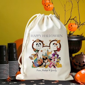 May include: A cream-colored drawstring bag with a Halloween-themed graphic. The design features Mickey and Minnie Mouse, along with other Disney characters, in front of a castle. The text "HAPPY HALLOWEEN" is printed above the graphic, and "From, Andrew & family" is printed below.
