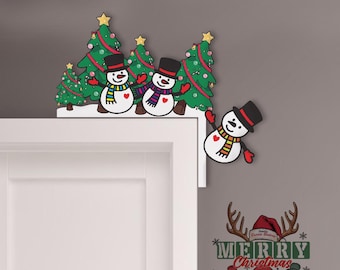 May include: A Christmas-themed door frame decoration featuring snowmen and Christmas trees. The snowmen wear black top hats, colorful scarves, and red gloves. The Christmas trees are green with red garland and gold star toppers.
