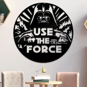 May include: Black circular wall art featuring Darth Vader's silhouette and the phrase "USE THE FORCE" in bold white letters. The design includes a detailed depiction of Vader's helmet and surrounding imagery.