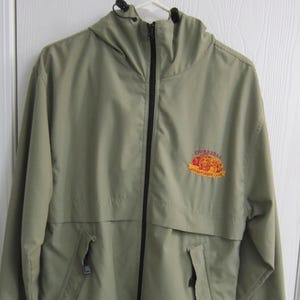 May include: Olive green hooded jacket with a black zipper and two front pockets. The jacket has a logo on the upper left chest that reads "ONBEBRAS Adventure Club". The jacket is hanging on a white hanger.