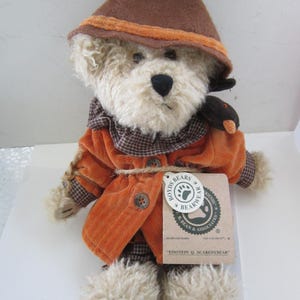 May include: A plush brown and orange scarecrow bear wearing a brown hat with an orange trim. The bear is holding a small black bird in its right paw. The bear has a tag that reads "BOYDS BEARS & BEARWEAR FRIENDS B. BEAN & ASSOCIATES" and "EINSTEIN Q. SCAREDYBEAR".