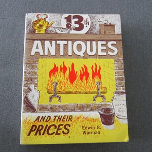May include: A vintage book cover titled "Antiques and Their Prices" with a yellow and brown design. The cover features illustrations of a fireplace, a teapot, and other antique items. The book is by Edwin G. Warman.