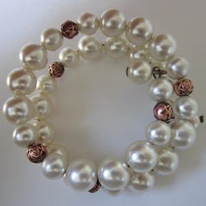 May include: A double-strand pearl bracelet with copper rose accents. The pearls are white and the roses are a reddish-brown color.